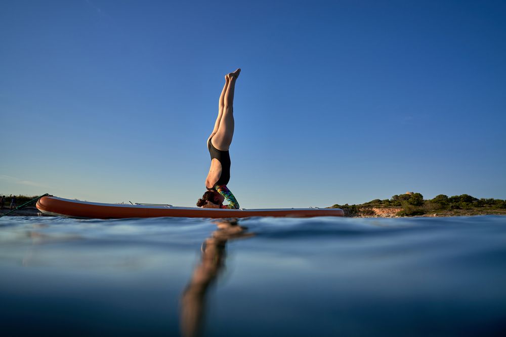 Unrecognizable woman practicing Supported Headstand on SUP board