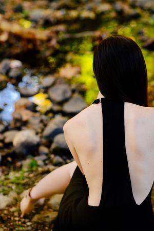 Back view of woman sitting near a creek in open backed dress in the fall