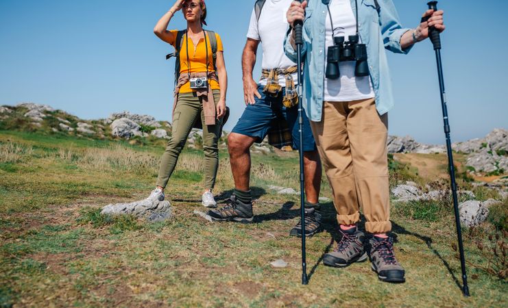 Three hikers with poles stopped looking at view on hill by ocean