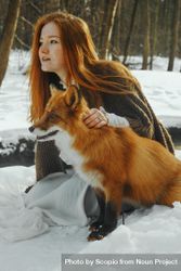 Young woman with red hair sitting on snow covered ground with a fox 4mwzN0