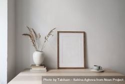 Elegant neutral poster mockup, picture frame on beige table with vase with dry grass 0v9ppb