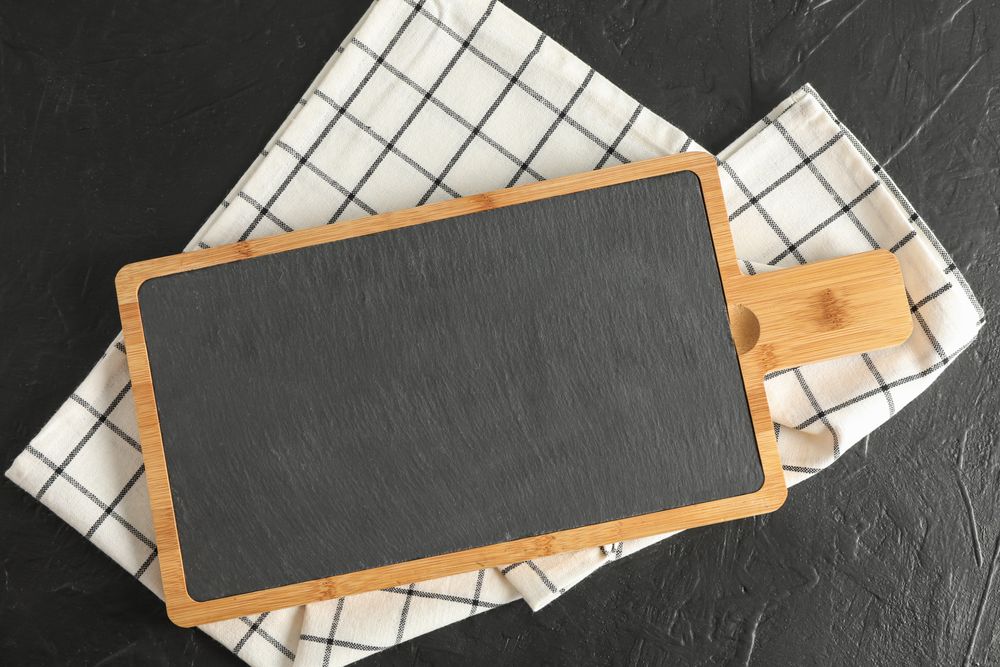 Cutting board with kitchen towel on dark background, top view