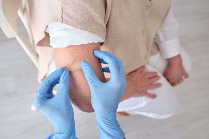 Crop medic applying sticking plaster on arm of patient