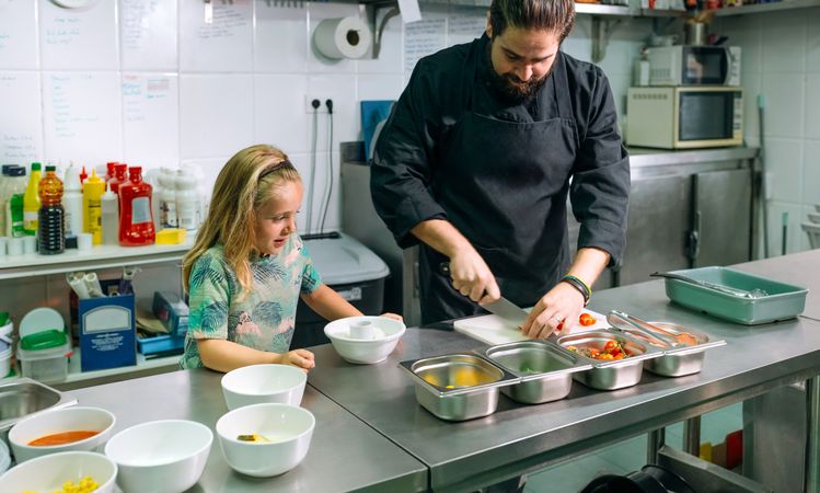 Chef preparing ingredients for poke bowl with little girl watching him in a professional kitchen