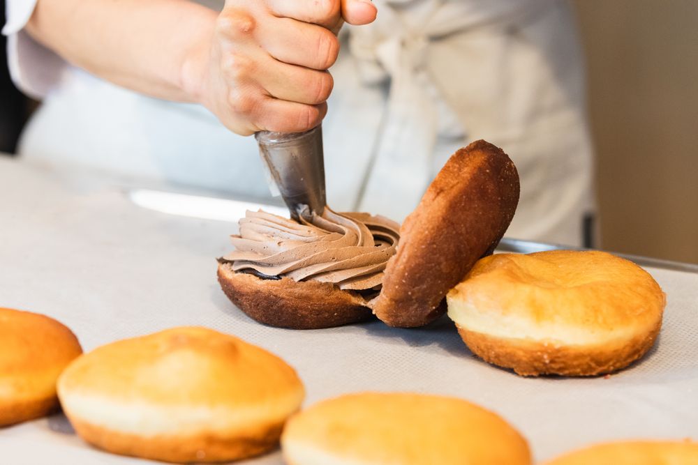 Unrecognizable baker adding cream on cakes in kitchen
