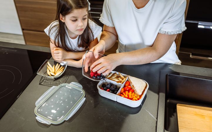 Girl watching her mother putting food in her lunch box