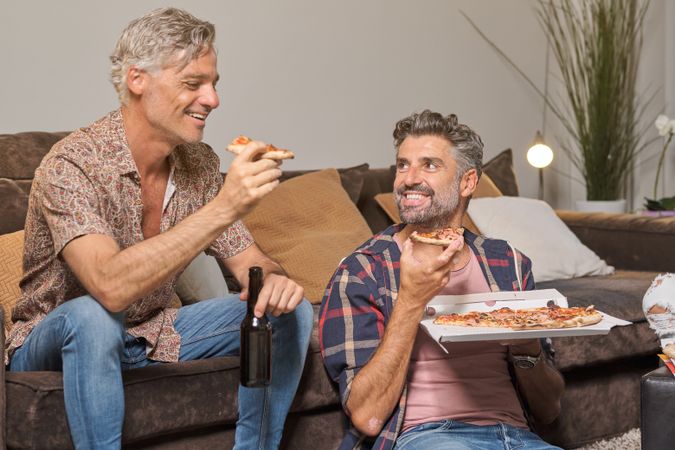 Cheerful male friends eating pizza at home