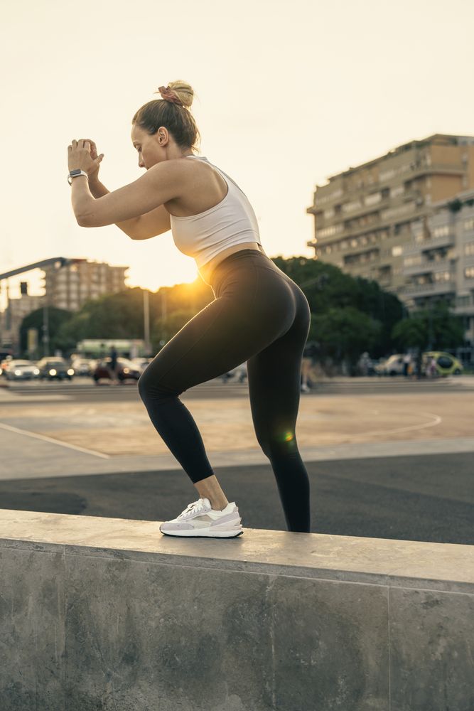 Athletic woman performing a step-up exercise during an outdoor urban workout at sunset