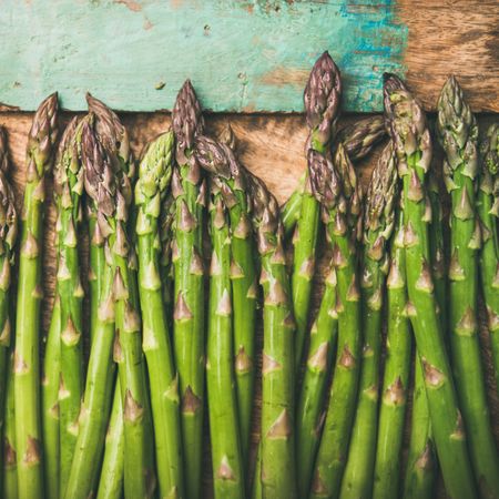 Asparagus laid on wooden board with green trim, square crop with copy space