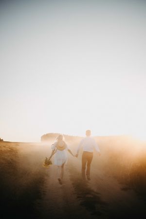 Back view of man and woman holding hands and walking on brown field