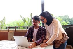 Two Young Asian Working People, Discussing at the Cafe Table, Working with Laptop Explaining File on Screen