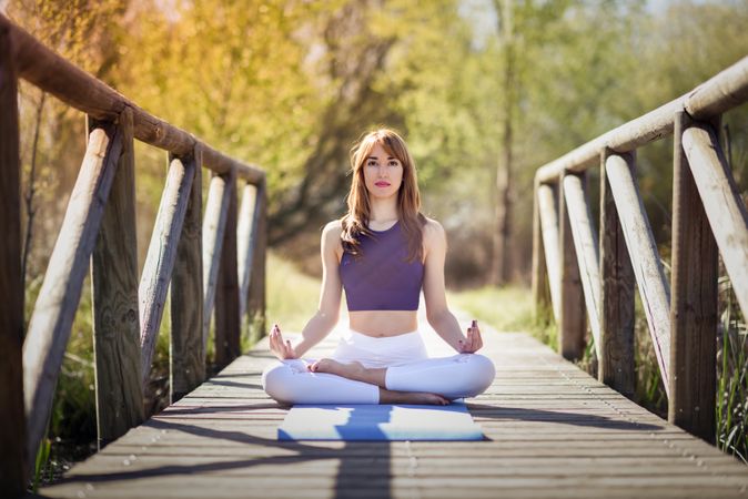 Woman wearing sport clothes meditating with eyes closed on yoga mat on forest path