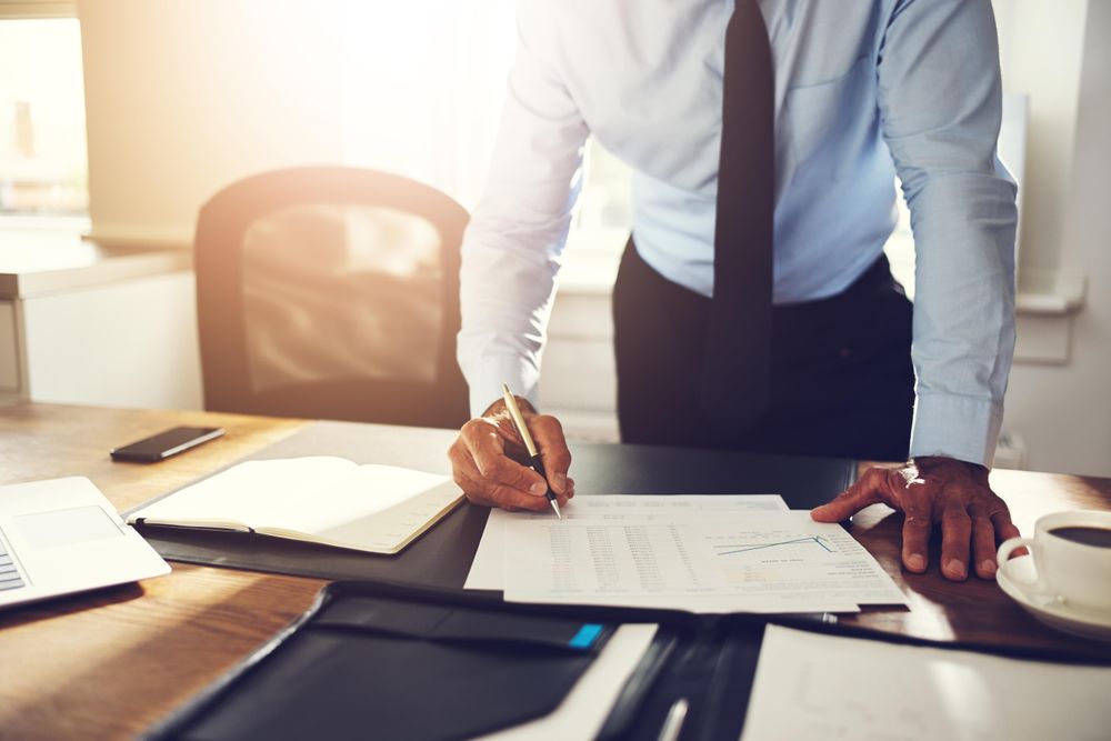 Man in business attire standing at his desk signing documents