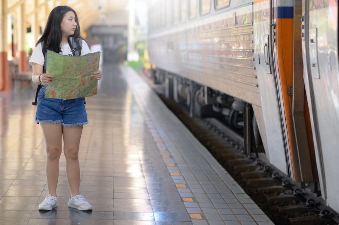 A young woman holding a map standing on the platform looking at the train