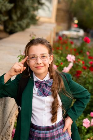 Girl in school uniform with hand raised to glasses