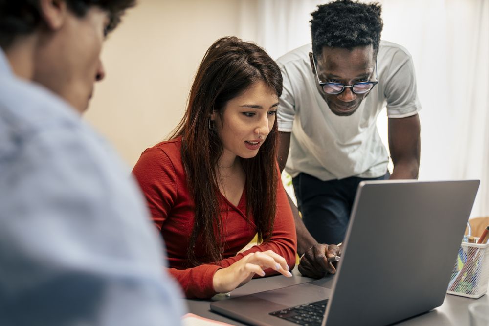 Diverse colleagues working together on a laptop in a modern office.