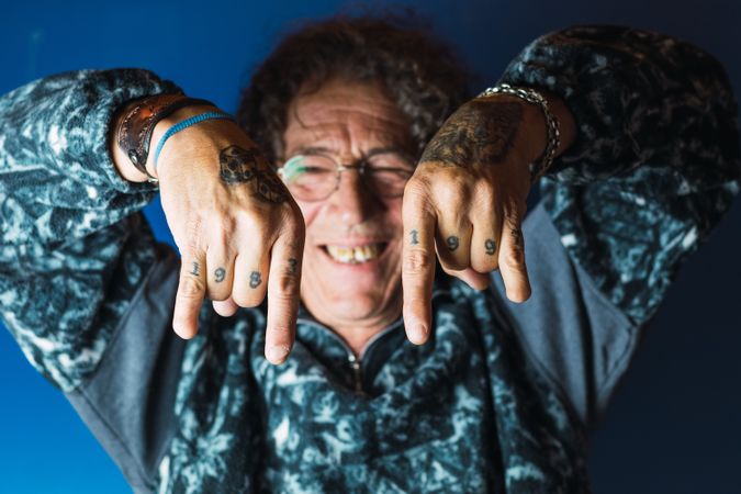 Positive tattooed mature man showing rock and roll gesture in studio