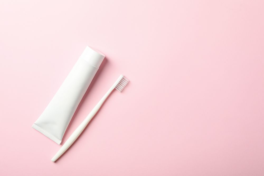 Toothbrush and toothpaste on pink background, space for text