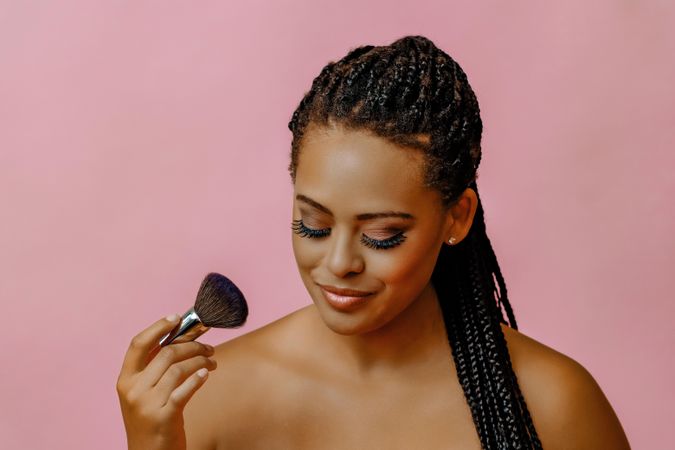 Female smiling and looking away with a make up brush in pink studio shoot