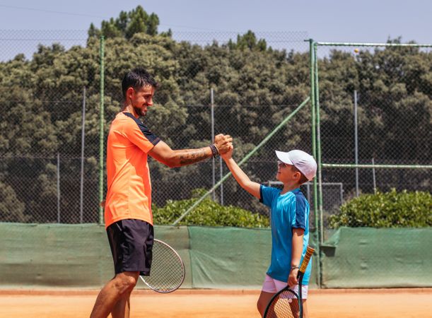 Father and son playing tennis together on a dirt court