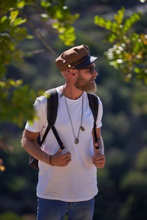 Bearded traveler with rucksack standing against mountain slope