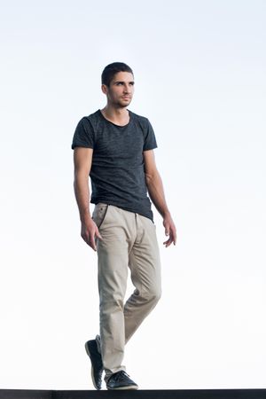Full body portrait of male in t-shirt and slacks on bright background, copy space