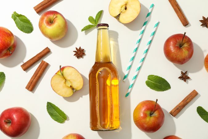 Composition with cider, apples, straws and cinnamon on blank background