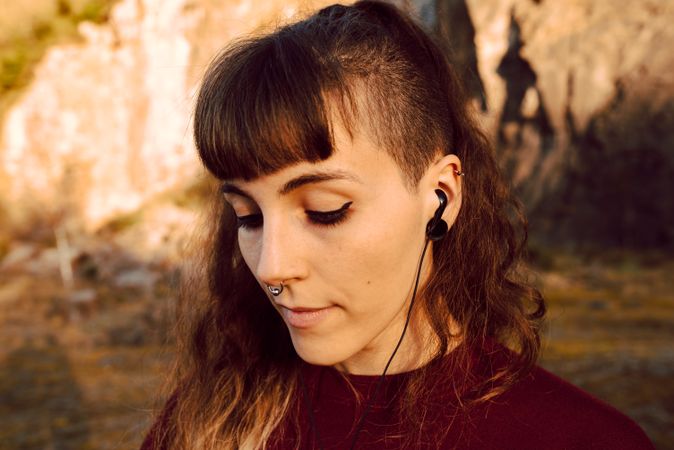 Young woman with piercing listening music on smartphone on hill
