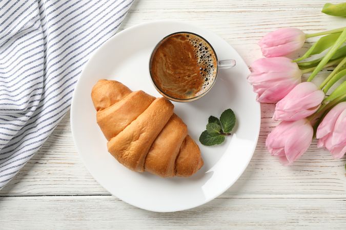 Top view of plate with croissant on wooden table with tulips