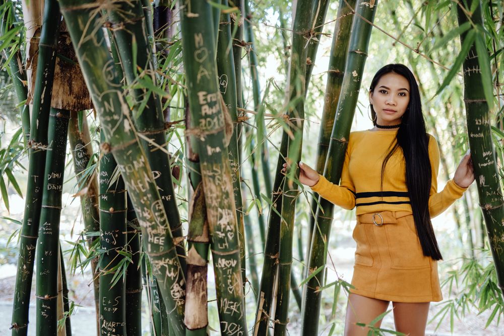 Stylish long haired Asian woman standing in park with flowers