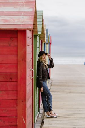 Stylish woman smiling and leaning on bright wooden cabins on beach
