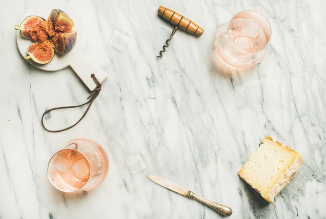 Two glasses of rose wine on marble table with quartered fig, cheese, knife, with copy space