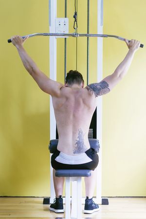 Back of tattooed male pulling down bar on weight machine