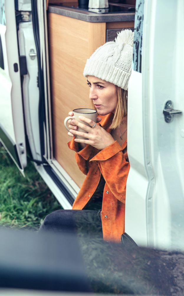 Female relaxing with coffee sitting on camper van step, close up vertical