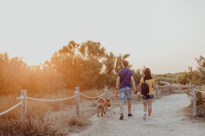 Casual adult couple walking with dog along rural pathway