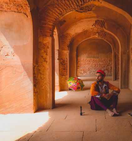 Man in traditional outfit sitting on floor in hallway and looking away
