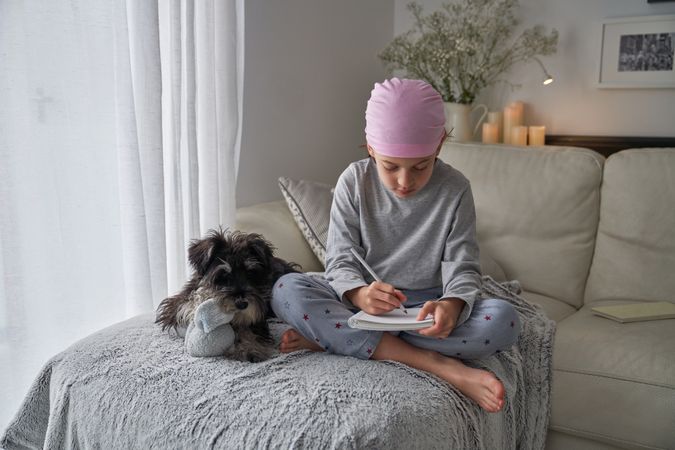 Boy in pink bandana writing in notepad near dog