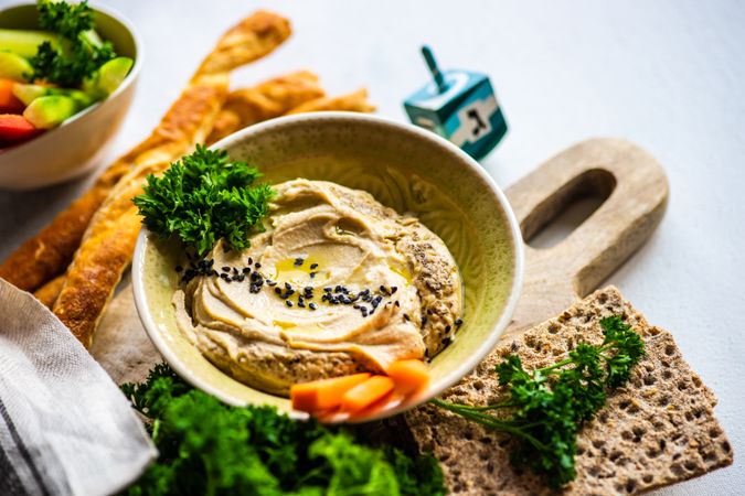 Creamy hummus dip in bowl on board served with veggies and crackers