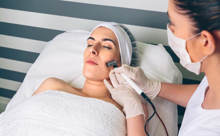 Woman receiving facial treatment on cheek in beauty center