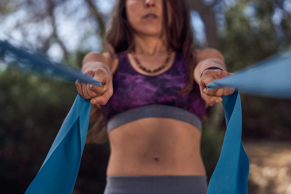 Crop fig woman exercising with ribbons during yoga session in na