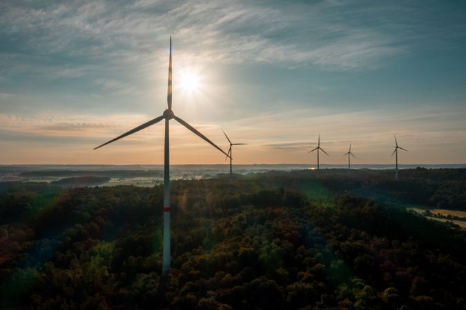 Drone shot with a multitude of wind turbines in the forest at sunrise in Germany