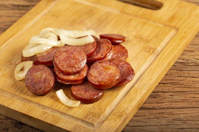 Sliced calabrese sausage with onion on wooden background.