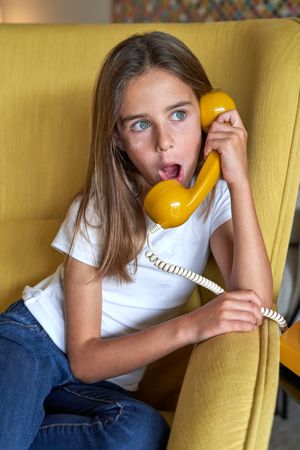Astonished girl talking on retro telephone in room