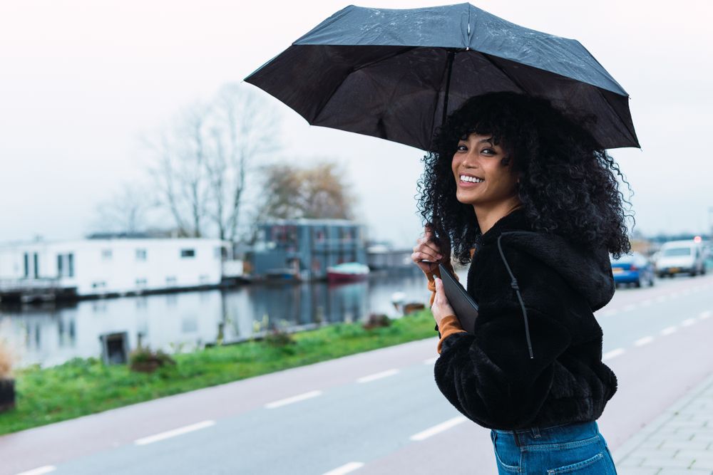 Smiling Black woman with umbrella on street