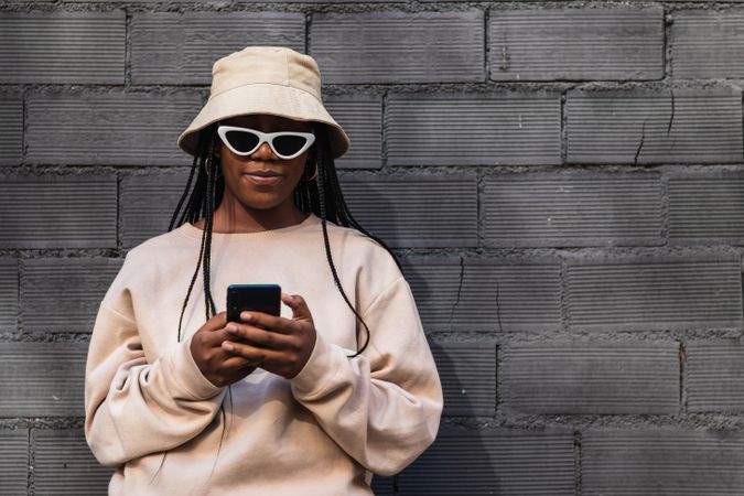 Black woman using smartphone near brick wall