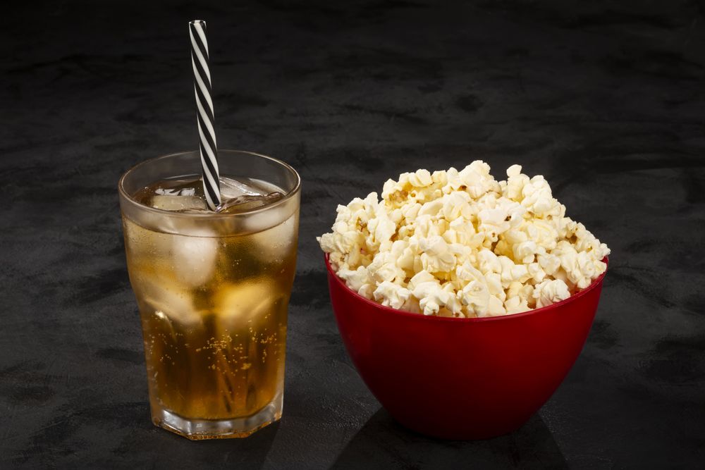Bowl with salted popcorn and soda on the table.