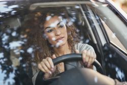 Serious female with curly hair sitting in car with hands on steering wheel
