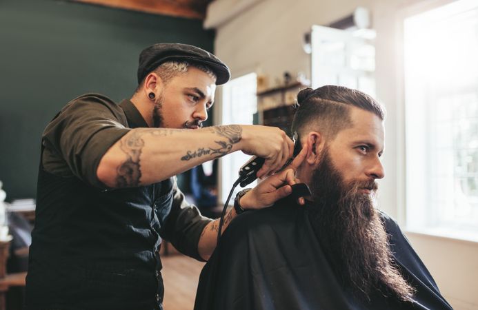 Young bearded man getting trendy haircut in barbershop