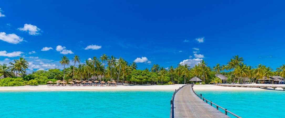 Walkway above brilliant blue water leading to beach, wide