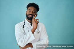 Thoughtful Black male doctor in blue studio with pen to his chin 41WoZ0